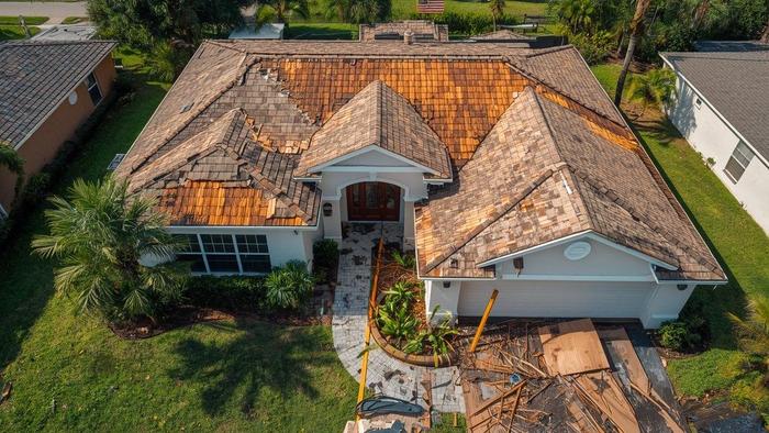 Storm-damaged roof on Florida stucco home after hurricane, missing shingles and debris visible