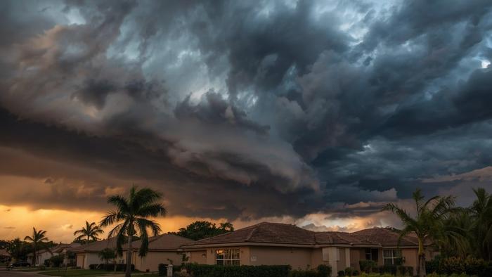 Dramatic storm clouds building over South Florida residential neighborhood with palm trees and stucco homes